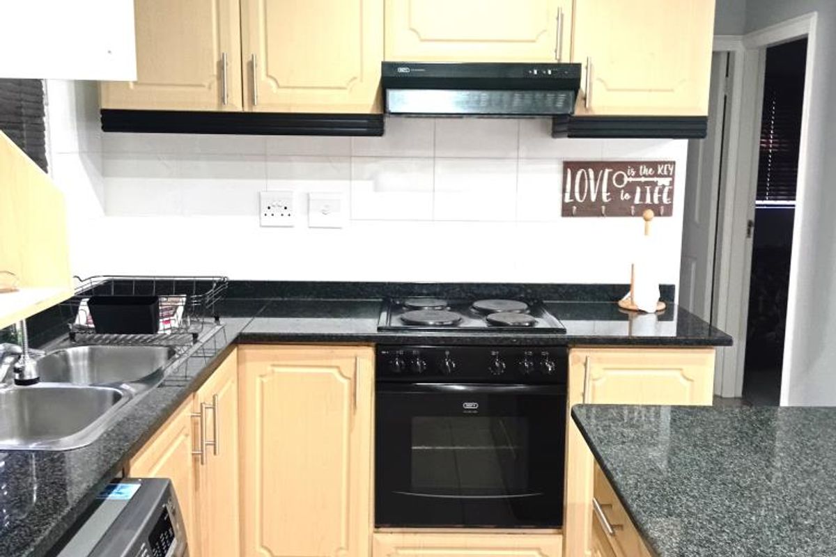A functional kitchen featuring light wood cabinetry, dark granite countertops, a built-in oven, hob, extractor fan, and integrated laundry appliance space.