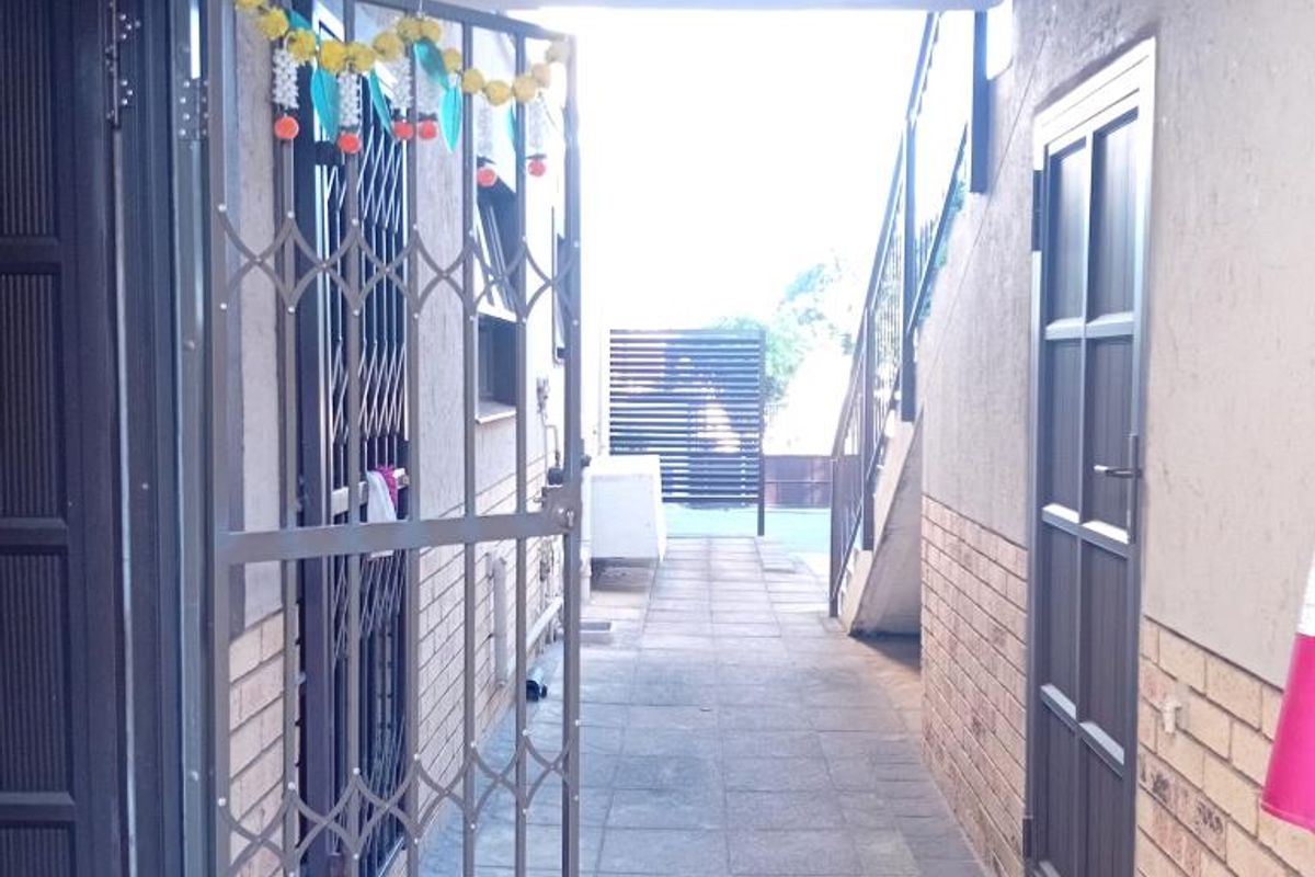 A covered exterior walkway featuring tiled flooring, brick accents, and security gates, providing access between apartment units.