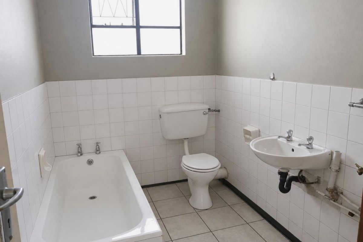 A functional bathroom featuring a standard bathtub, wall-mounted basin, and toilet with tiled flooring and partial wall tiling.