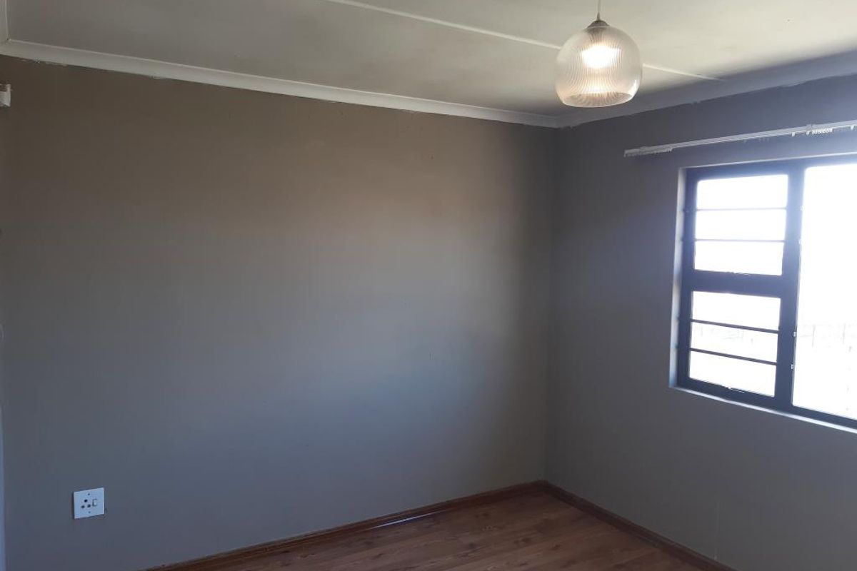 A vacant bedroom featuring laminate wood flooring, neutral grey walls, and a single window with a curtain rail.