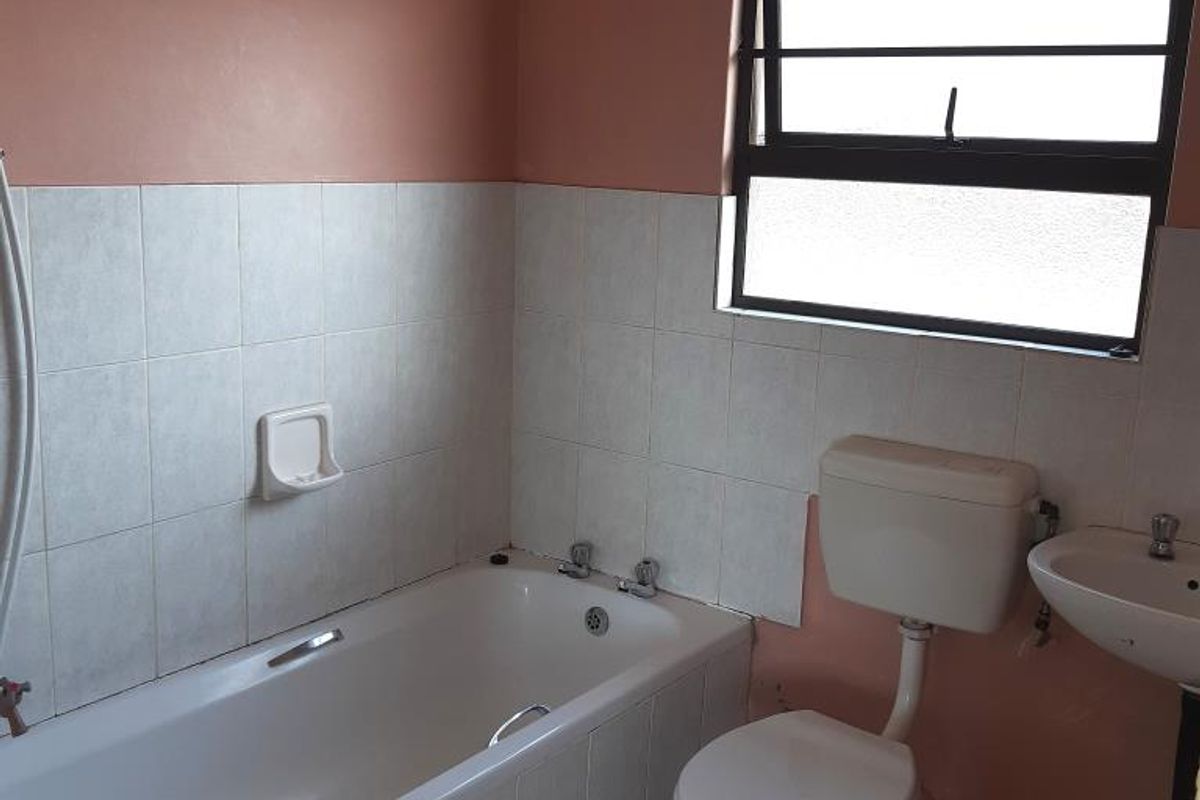 A functional bathroom featuring a standard bathtub, toilet, and wall-mounted basin with tiled splashbacks and a window for natural light.