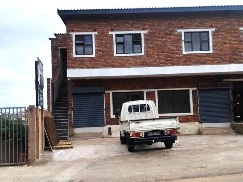 Front elevation of a two-story face brick commercial or apartment building featuring security roller shutters, an external staircase, and gated perimeter access.