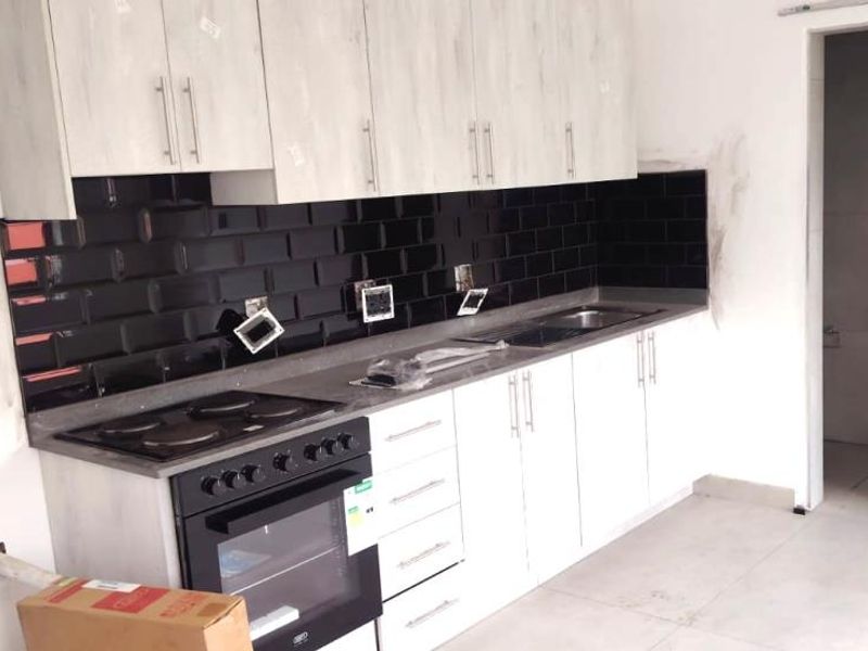 A modern kitchen featuring white cabinetry, black subway tile backsplash, and built-in appliances, currently undergoing final finishing touches.