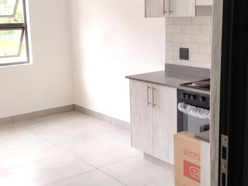 A modern, empty kitchen featuring light-toned cabinetry, a tiled backsplash, and built-in oven and hob, set against neutral tiled flooring.