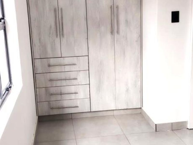 A bright, empty bedroom featuring modern light-wood grain built-in wardrobes and neutral floor tiles.