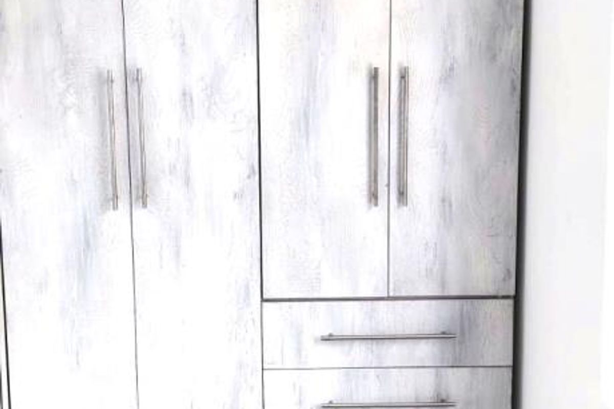 A clean bedroom space featuring a modern, light-toned built-in wardrobe with integrated drawers and neutral floor tiling.