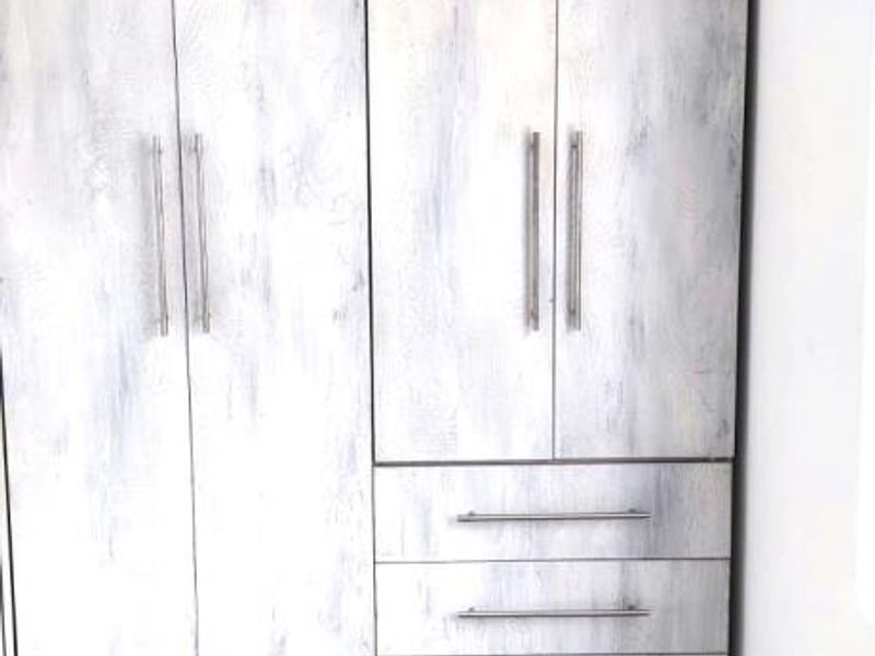 A clean bedroom space featuring a modern, light-toned built-in wardrobe with integrated drawers and neutral floor tiling.