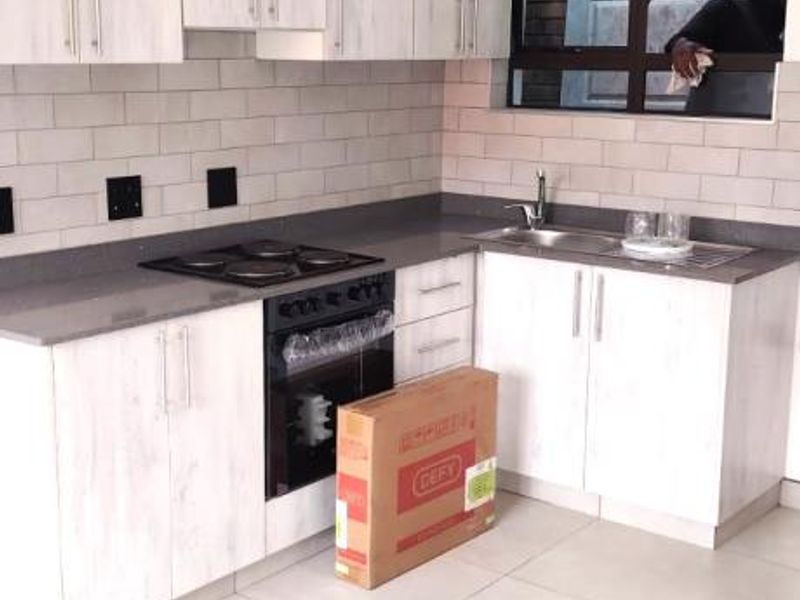 Modern kitchen featuring light wood-grain cabinetry, stone countertops, subway tile backsplash, and integrated oven and hob.