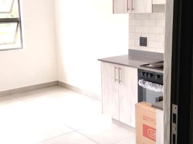 A modern, minimalist kitchen featuring light wood-grain cabinetry, subway tile backsplash, and tiled flooring, presented in a clean, empty state.
