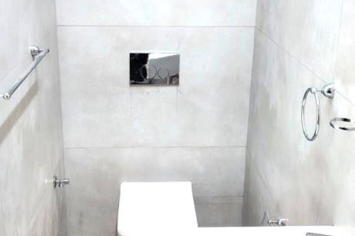A modern, minimalist guest bathroom featuring a wall-mounted toilet, sleek basin with chrome fixtures, and neutral large-format wall and floor tiles.
