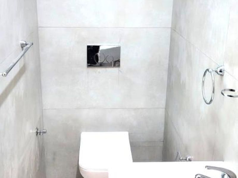 A modern, minimalist guest bathroom featuring a wall-mounted toilet, sleek basin with chrome fixtures, and neutral large-format wall and floor tiles.
