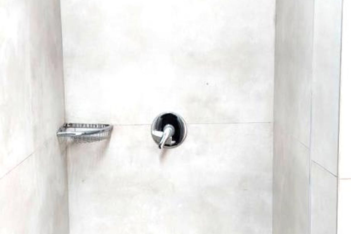 A clean, modern shower enclosure featuring neutral large-format wall tiles, a built-in soap dish, and a minimalist chrome shower fixture.