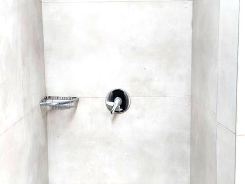 A clean, modern shower enclosure featuring neutral large-format wall tiles, a built-in soap dish, and a minimalist chrome shower fixture.