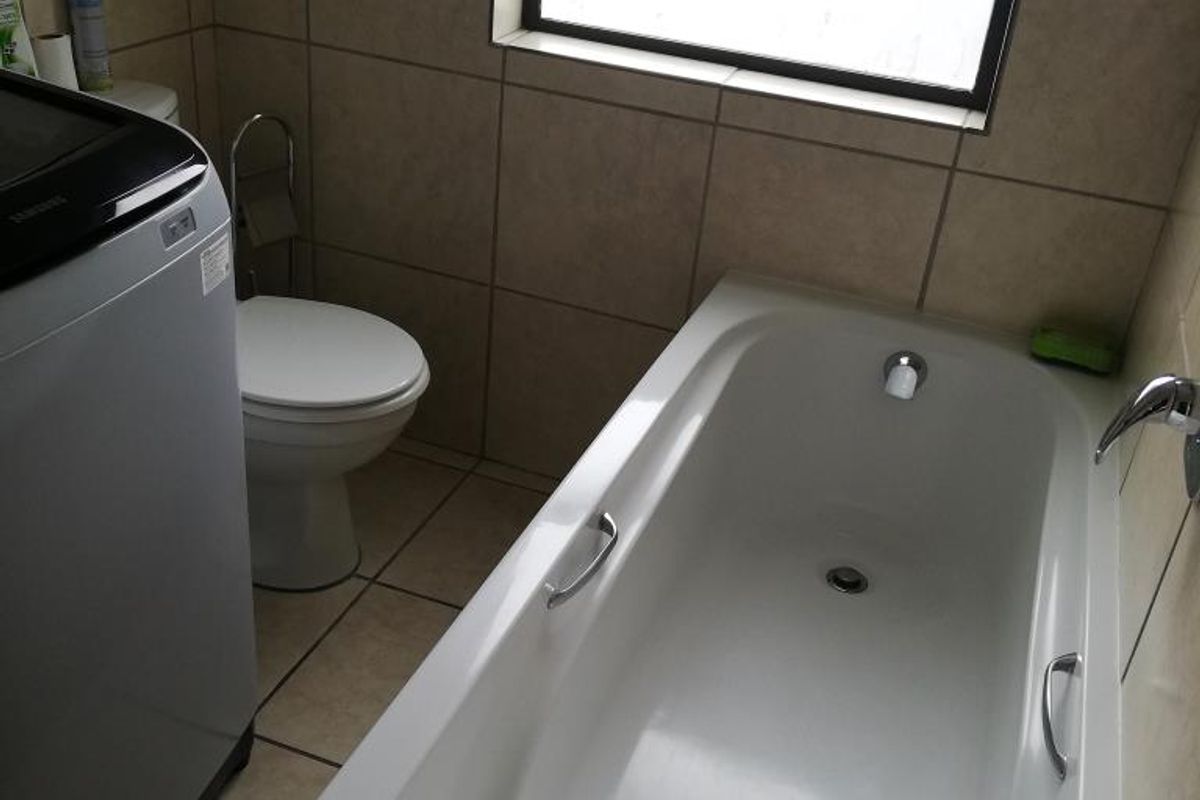 A functional bathroom featuring a built-in bathtub, a toilet, and tiled walls, with space provided for a laundry appliance.