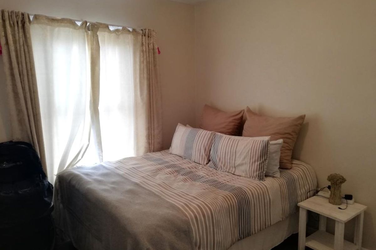 A cozy bedroom featuring neutral wall tones and natural light filtering through window treatments.