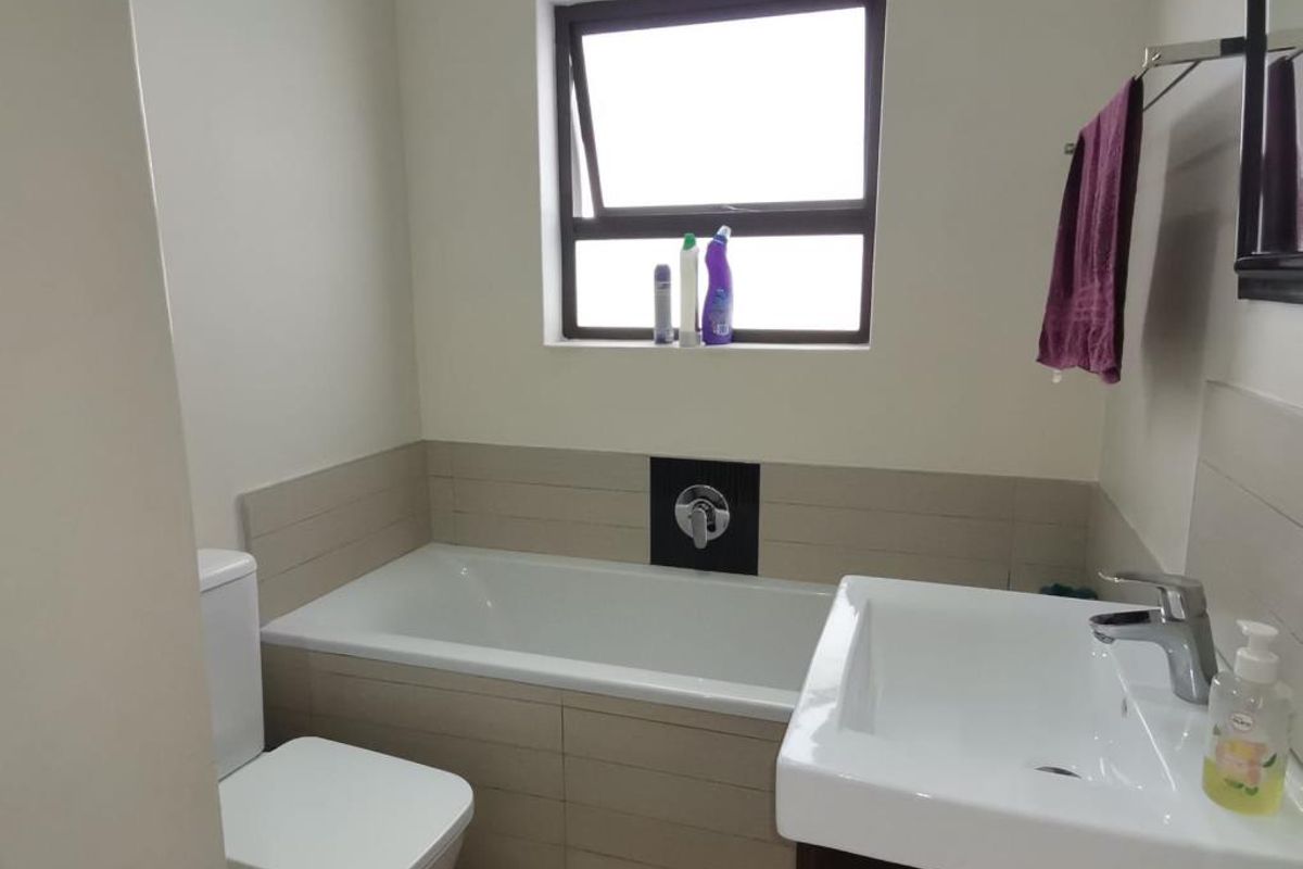 A functional bathroom featuring a built-in bathtub with tiled surround, a modern vanity basin, and a toilet.