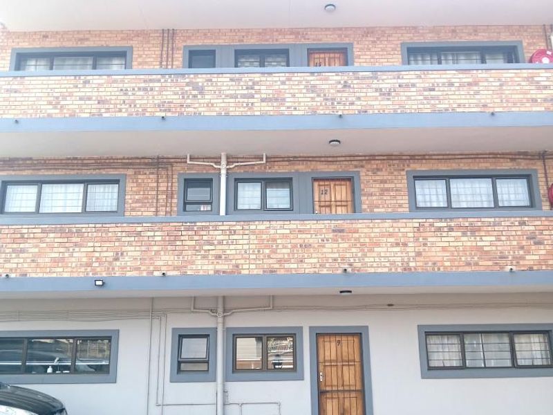 Front elevation of a multi-story apartment building featuring face brick construction, paved parking area, and secure access points.