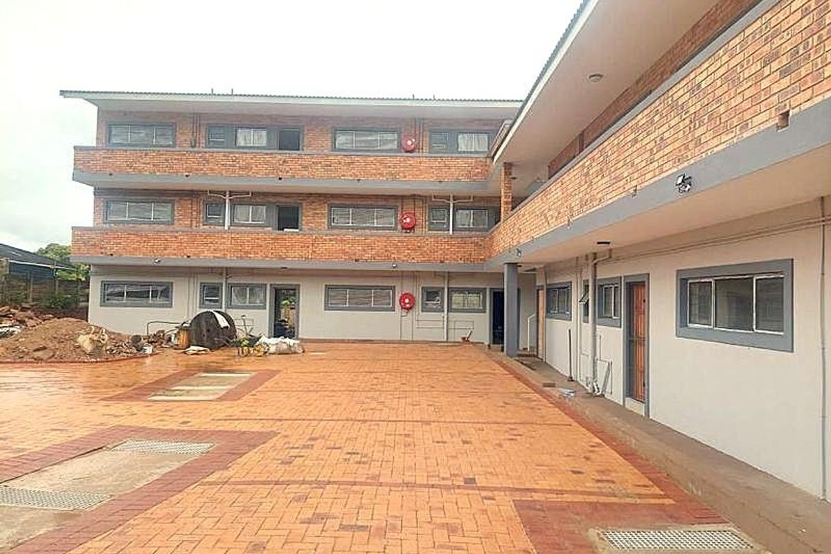 Exterior view of a multi-story apartment building featuring a face brick facade and a paved courtyard area with integrated drainage.