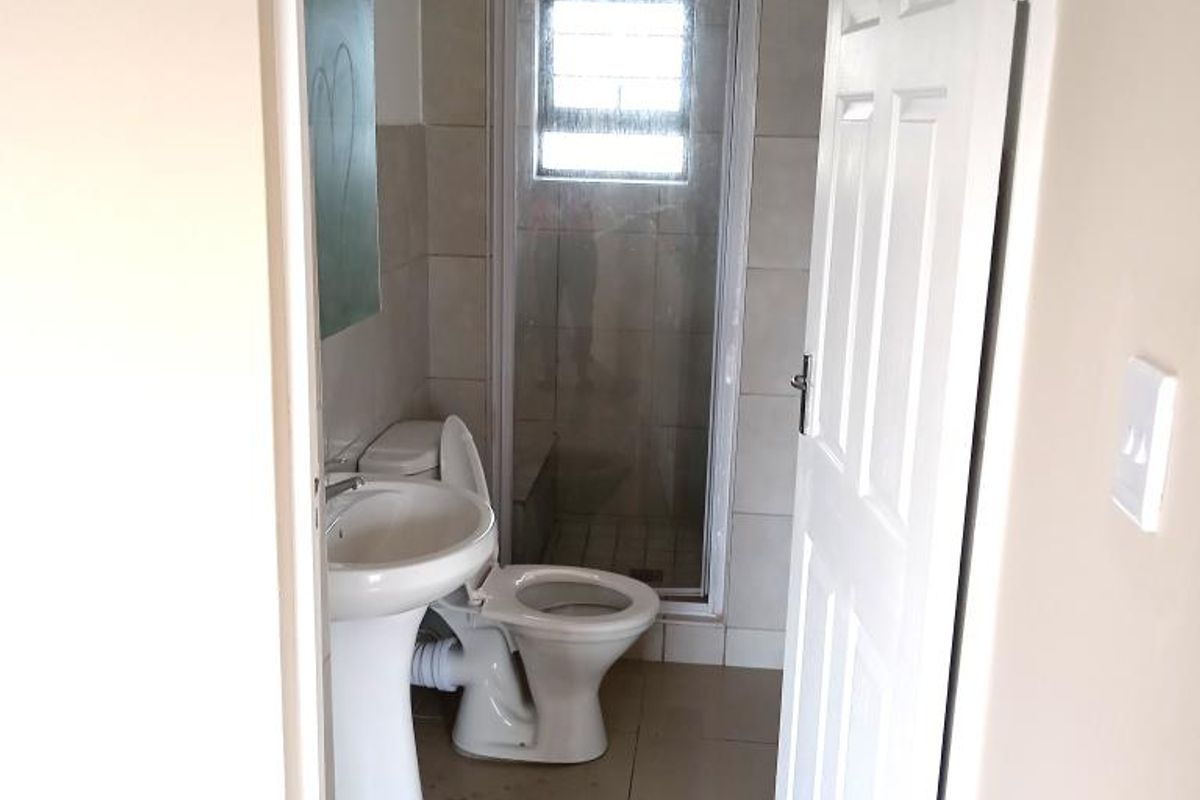A compact bathroom featuring a pedestal basin, toilet, and a glass-enclosed shower with tiled finishes.