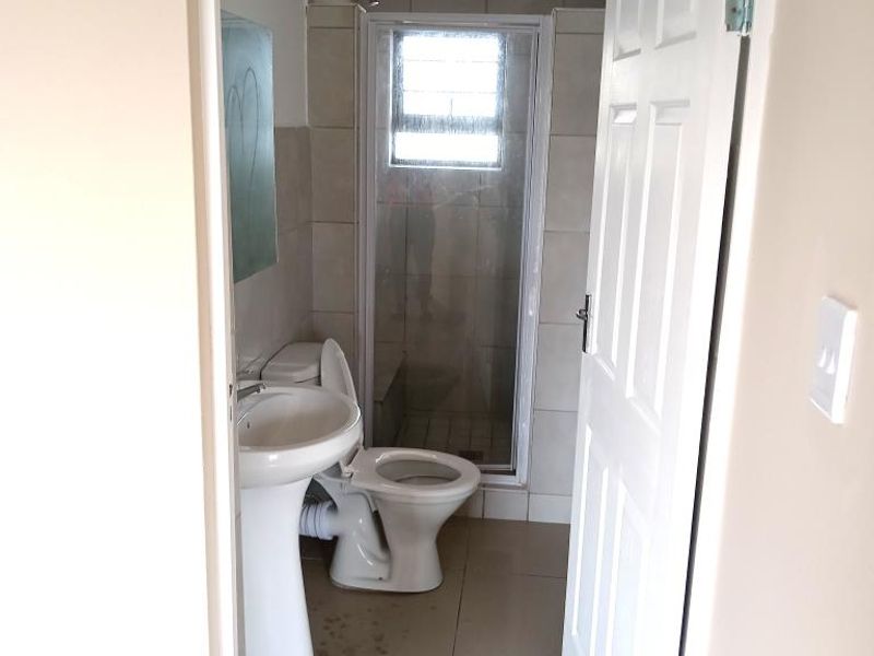 A compact bathroom featuring a pedestal basin, toilet, and a glass-enclosed shower with tiled finishes.