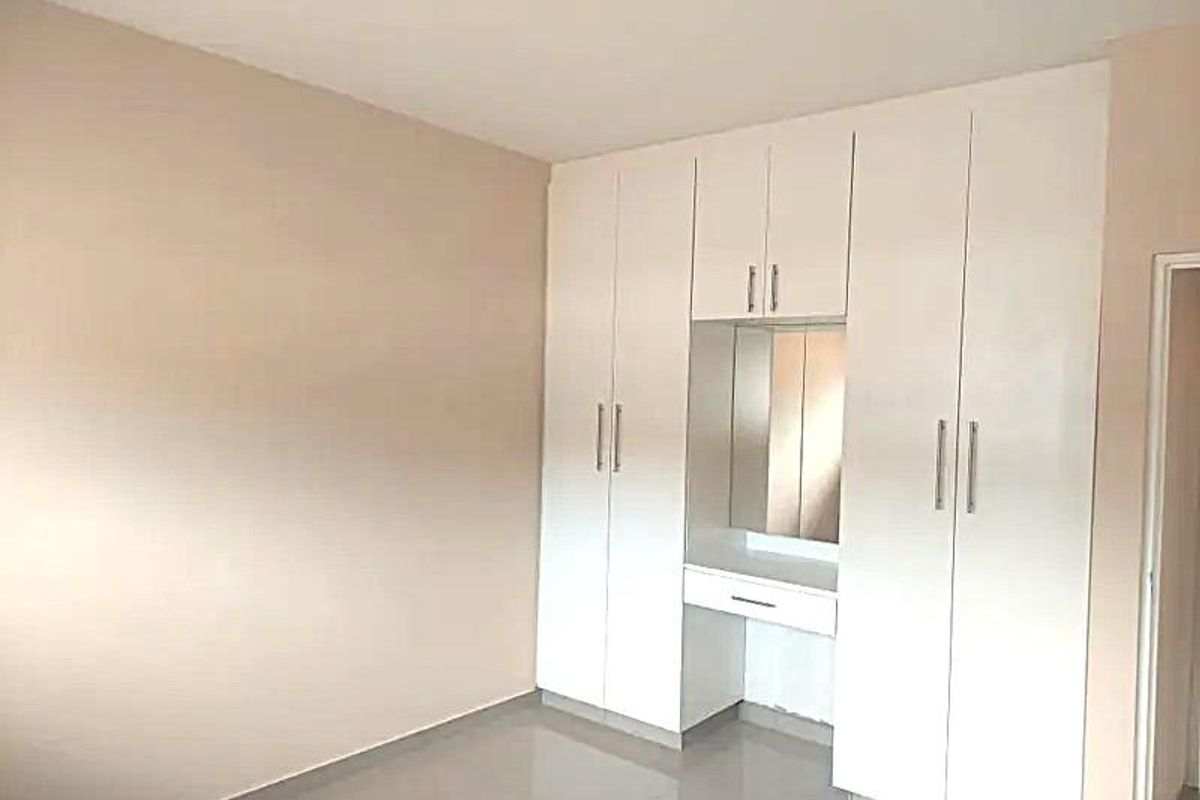 A clean, empty bedroom featuring white built-in cupboards with an integrated vanity area and neutral tiled flooring.