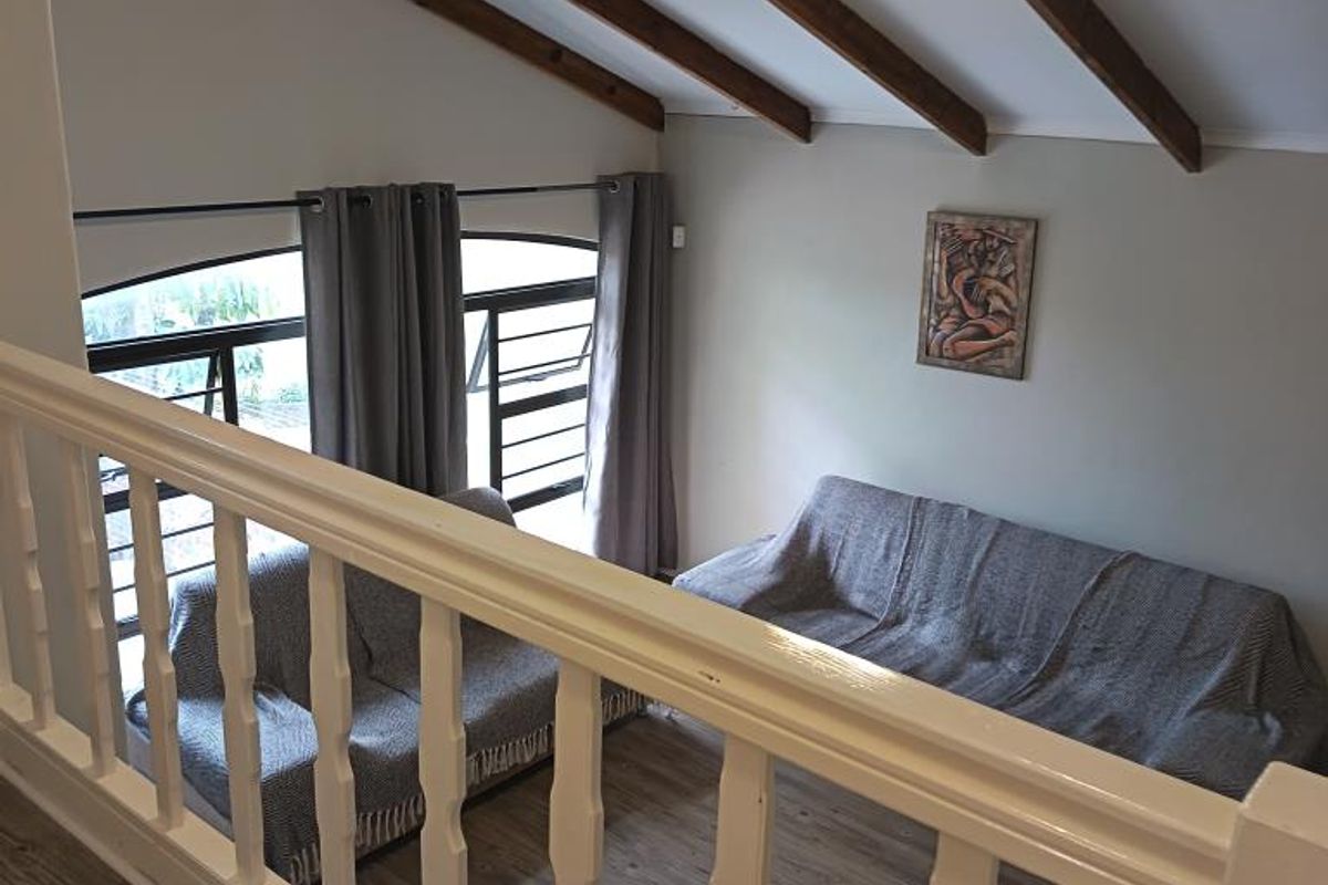 A view from a mezzanine level overlooking a living area featuring exposed timber ceiling beams, laminate flooring, and a white balustrade.