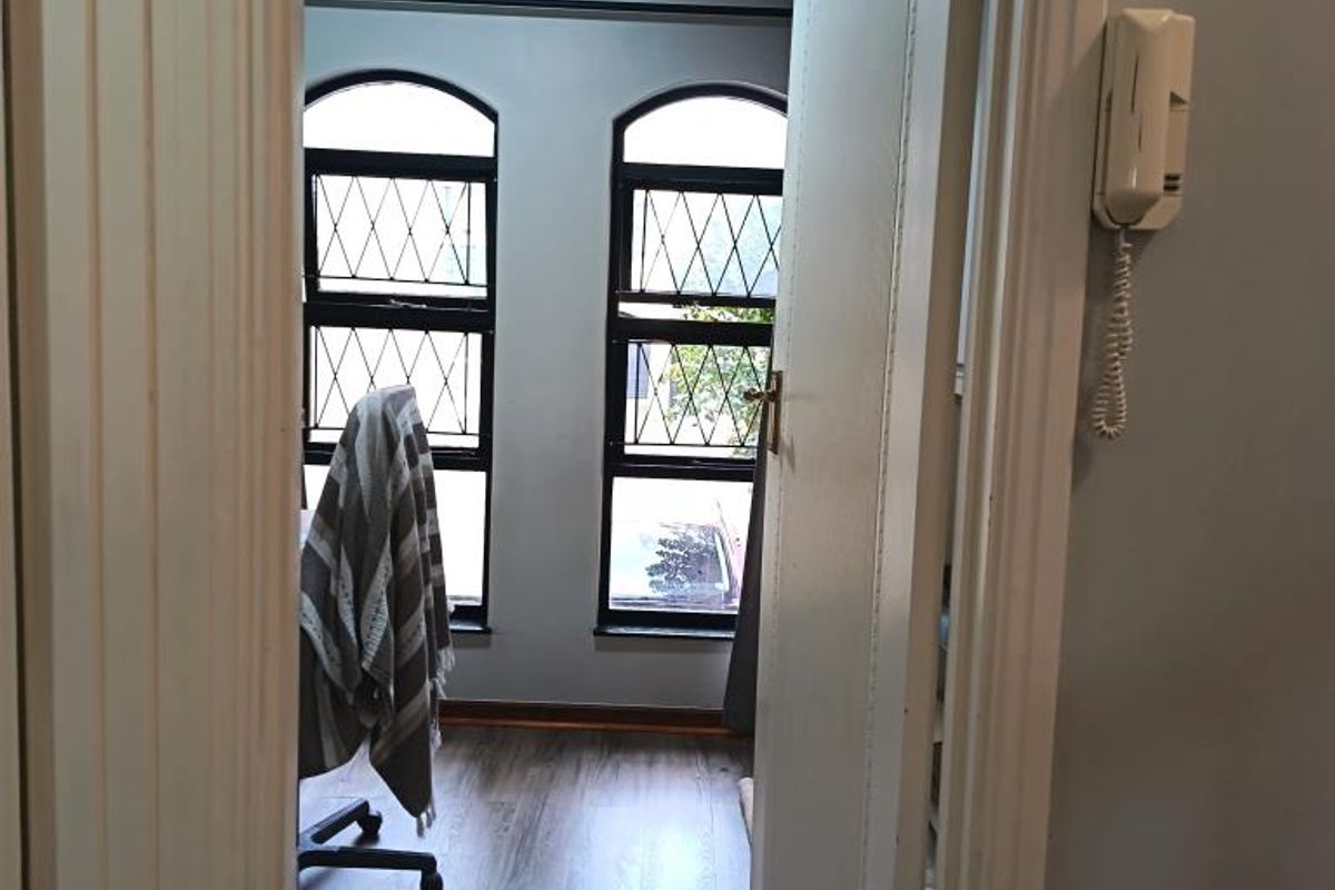 A view through a doorway into a room featuring arched windows with security bars and wood-look flooring.