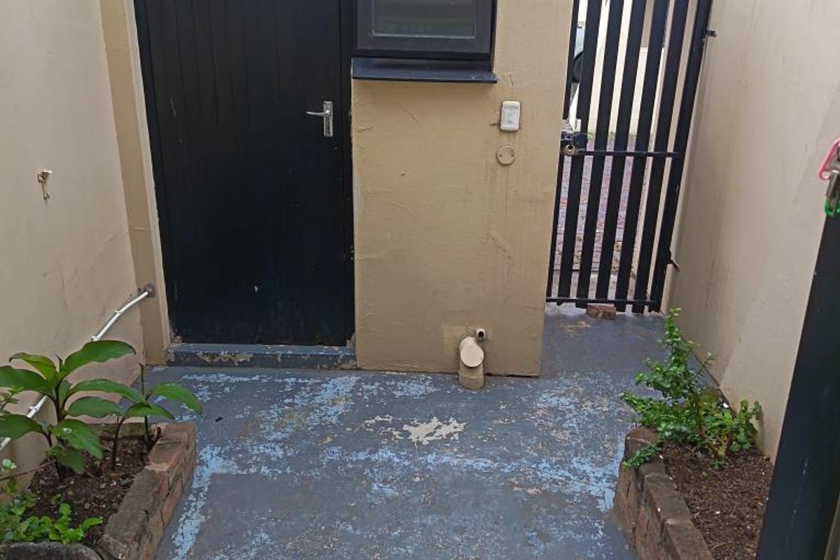 A small, enclosed rear courtyard area featuring a utility door, a small window, and brick-edged garden beds with a concrete floor.