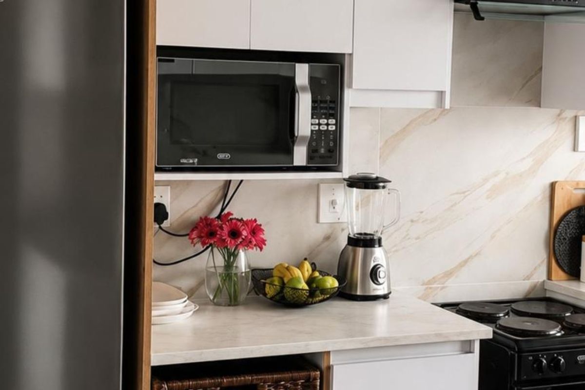 A modern kitchen area featuring white cabinetry, a marble-look backsplash, built-in microwave, and an electric stove with an extractor fan.