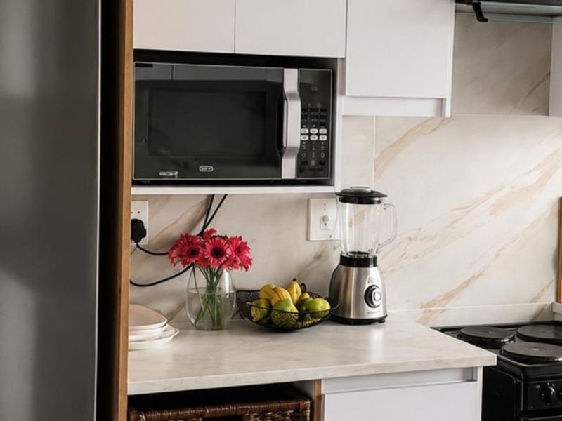 A modern kitchen area featuring white cabinetry, a marble-look backsplash, built-in microwave, and an electric stove with an extractor fan.