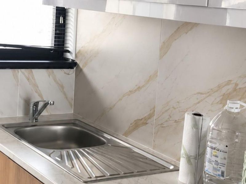 A clean kitchen area featuring a stainless steel sink, marble-look tiled splashback, and modern cabinetry with ample counter space.
