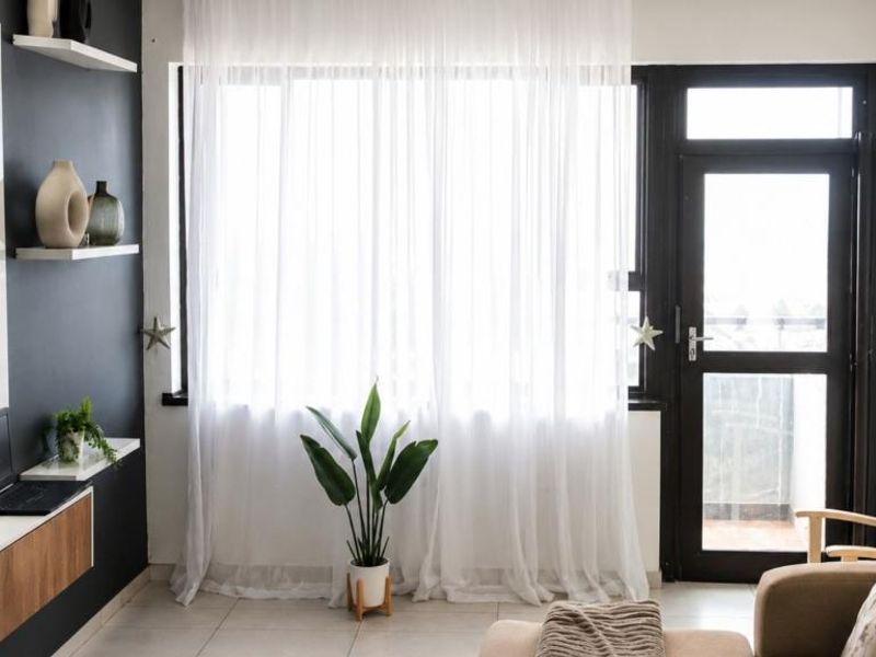 A bright living room featuring tiled flooring, floating wall shelves, and a glass door providing access to an outdoor area.