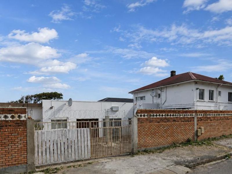 Front exterior view of the property featuring a brick perimeter wall with razor wire security, a metal gate, and a tiled roof structure.
