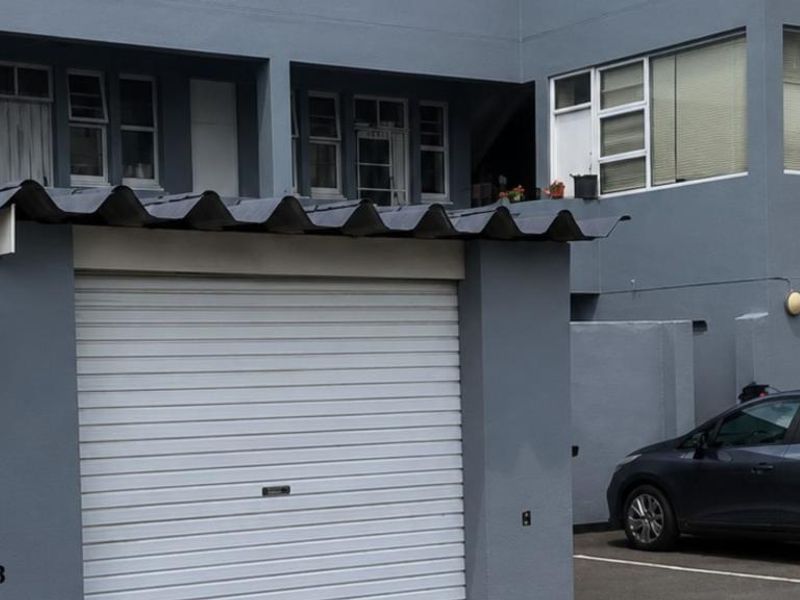 Exterior view of the apartment building featuring a roller garage door and grey painted facade with casement windows.