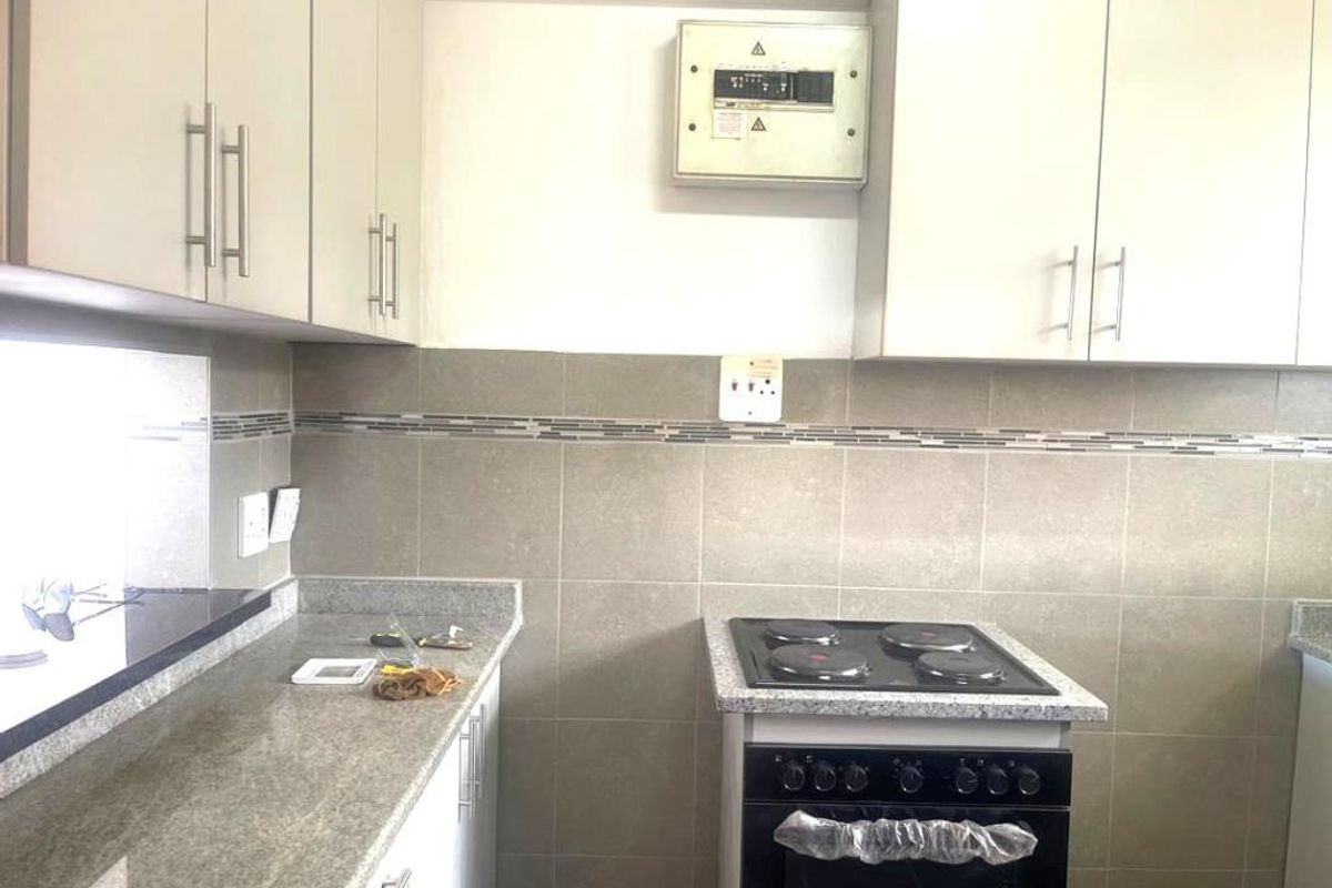 A functional kitchen featuring granite countertops, tiled backsplash, built-in cabinetry, and a freestanding electric stove.