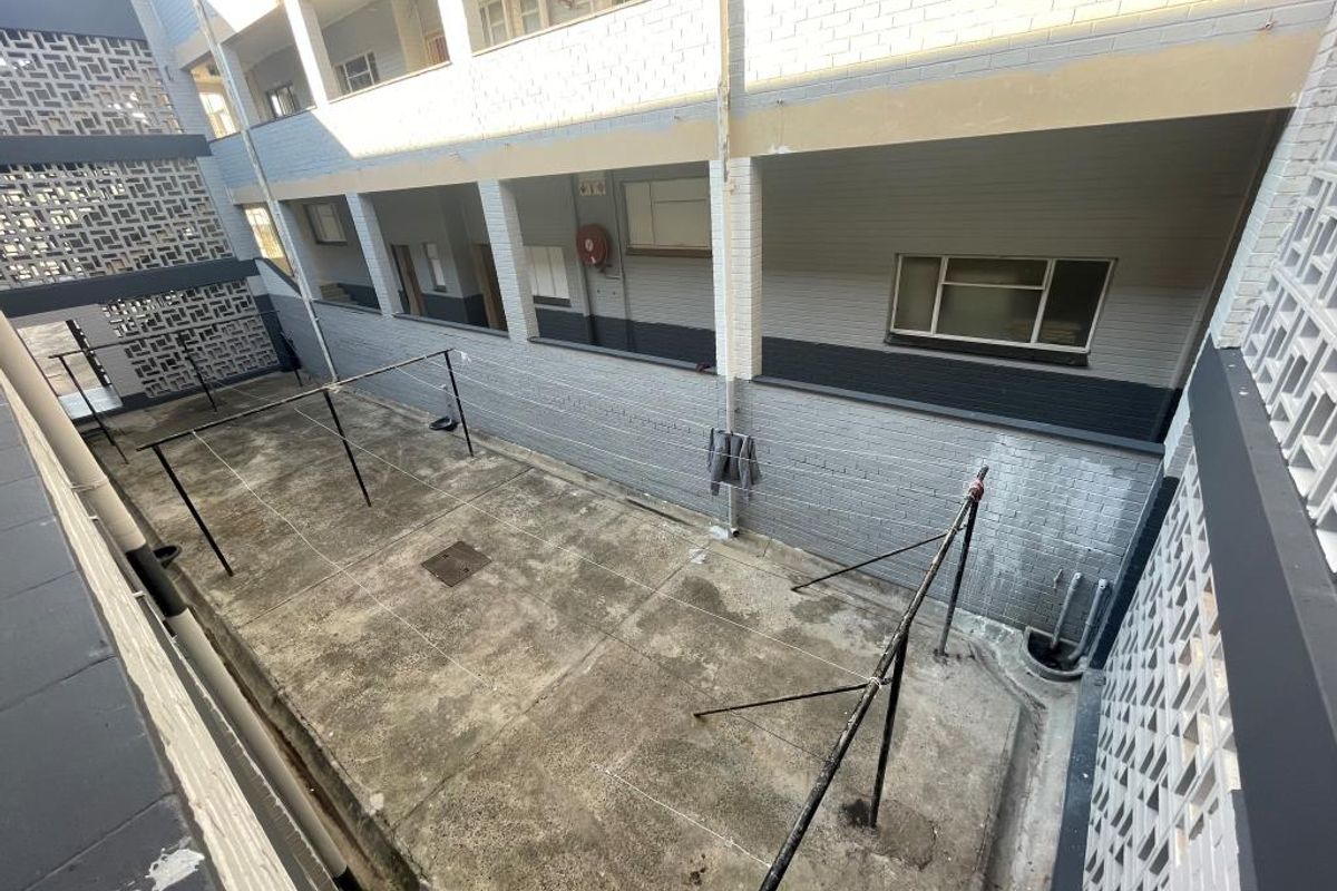An exterior view of a communal apartment courtyard featuring concrete flooring, metal clothes drying lines, and decorative breeze block wall detailing.