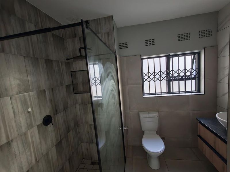 Modern bathroom featuring a floating vanity with a vessel sink, marble-look wall tiles, and a secure window with burglar bars.