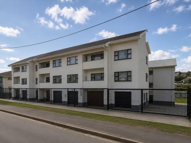 A multi-story apartment complex featuring a secure perimeter fence, ground-level garage access, and private balconies for each unit.