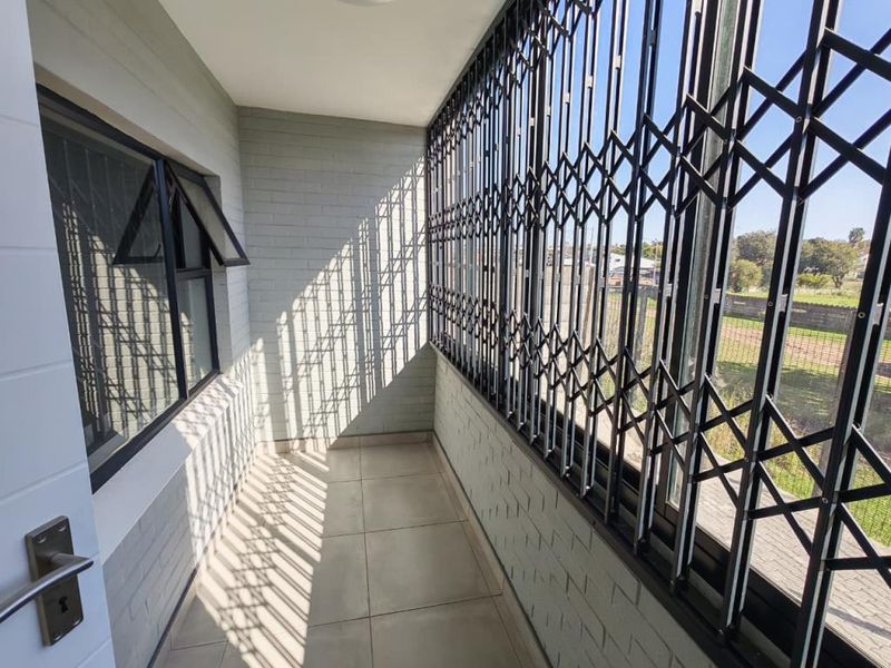 A clean, covered balcony featuring tiled flooring, brick walls, and a full-length security gate, offering a secure outdoor space.