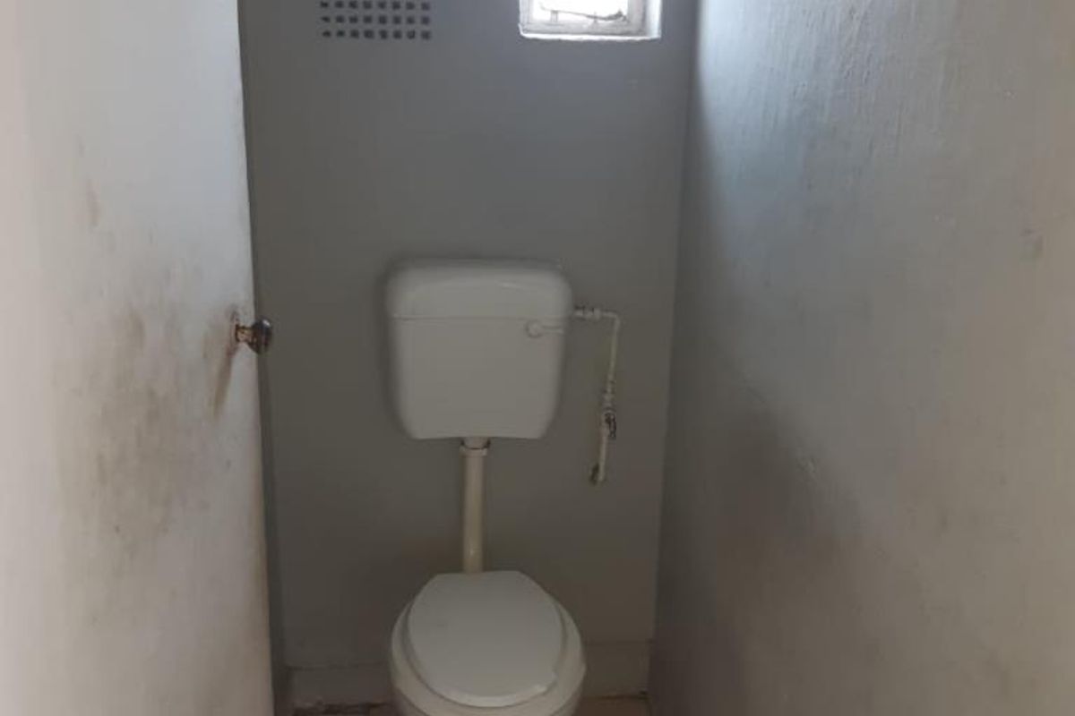 A small, basic bathroom featuring a standard toilet, tiled flooring, and a small window. The space requires cosmetic updates and repairs.