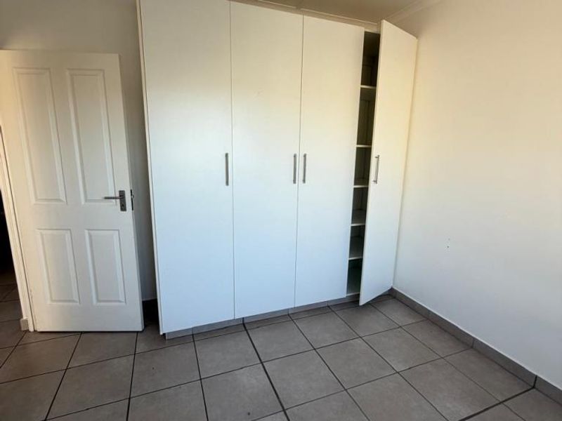 A bedroom featuring neutral floor tiles and a built-in white wardrobe with multiple storage compartments.