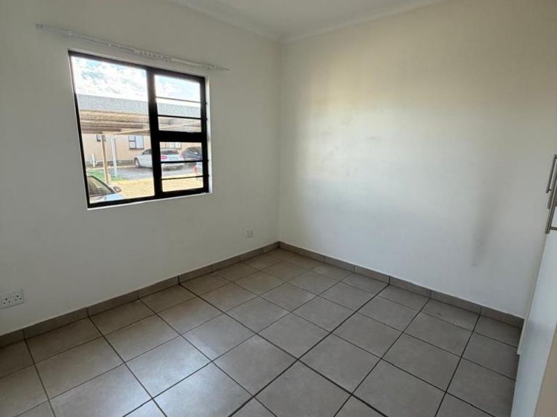 A bright, empty bedroom featuring neutral floor tiles, a large window with security bars, and built-in cupboard space.