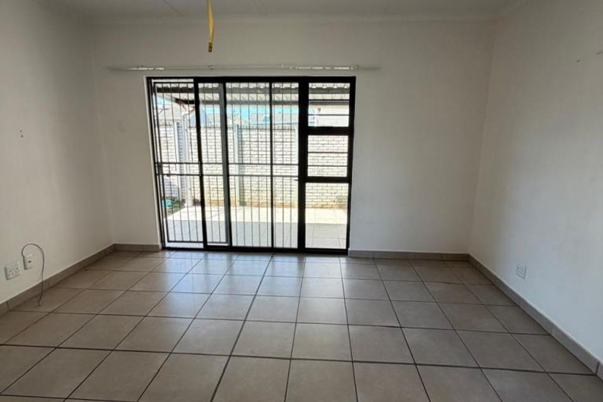 An empty living room featuring neutral floor tiles, a sliding glass door with security gate, and direct access to an outdoor patio area.