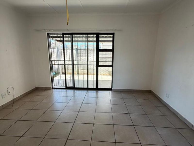 An empty living room featuring neutral floor tiles, a sliding glass door with security gate, and direct access to an outdoor patio area.
