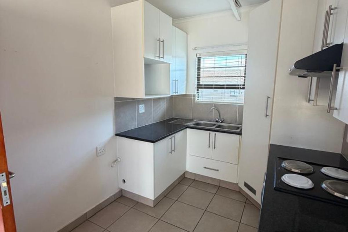 Compact kitchen featuring white cabinetry, dark countertops, tiled flooring, a built-in hob, and an extractor fan.