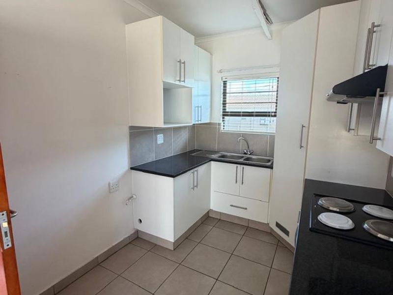 Compact kitchen featuring white cabinetry, dark countertops, tiled flooring, a built-in hob, and an extractor fan.