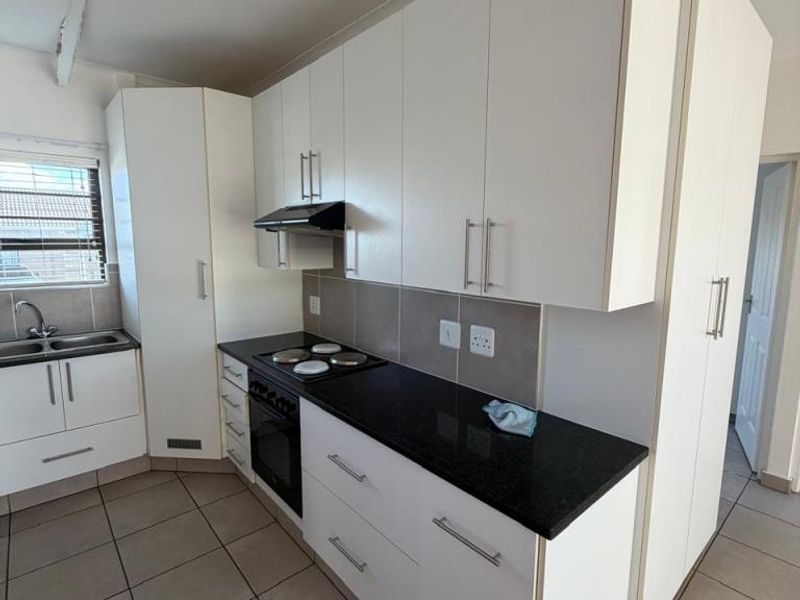 A functional kitchen featuring white cabinetry, dark countertops, a built-in oven with hob, extractor fan, and tiled flooring.