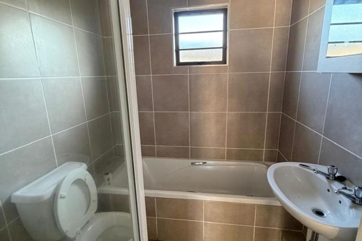 A functional bathroom featuring a built-in bathtub, a wall-mounted basin, and a separate shower enclosure with tiled walls and flooring.