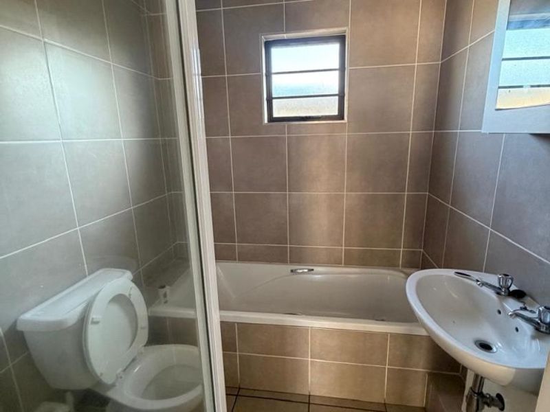 A functional bathroom featuring a built-in bathtub, a wall-mounted basin, and a separate shower enclosure with tiled walls and flooring.