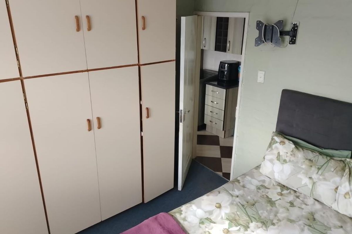 Bedroom featuring extensive built-in cupboard storage and a wall-mounted television bracket, with direct access to an adjacent kitchen area.
